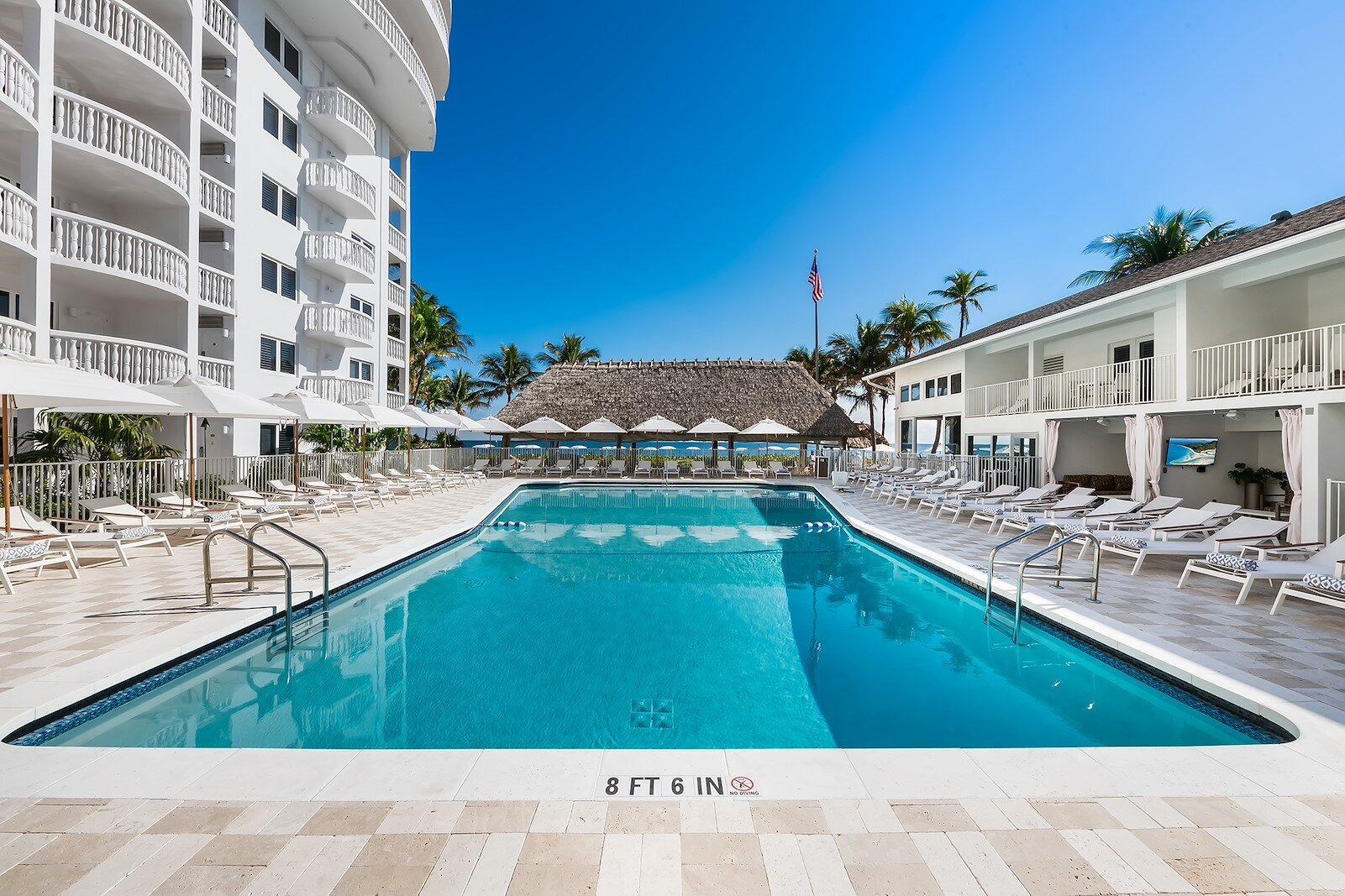 A large rectangular pool with lounge chairs and a thatched roof in the background.