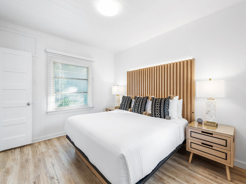 A wide view of a clean and modern guest room with a large bed, wooden headboard, and nightstands.