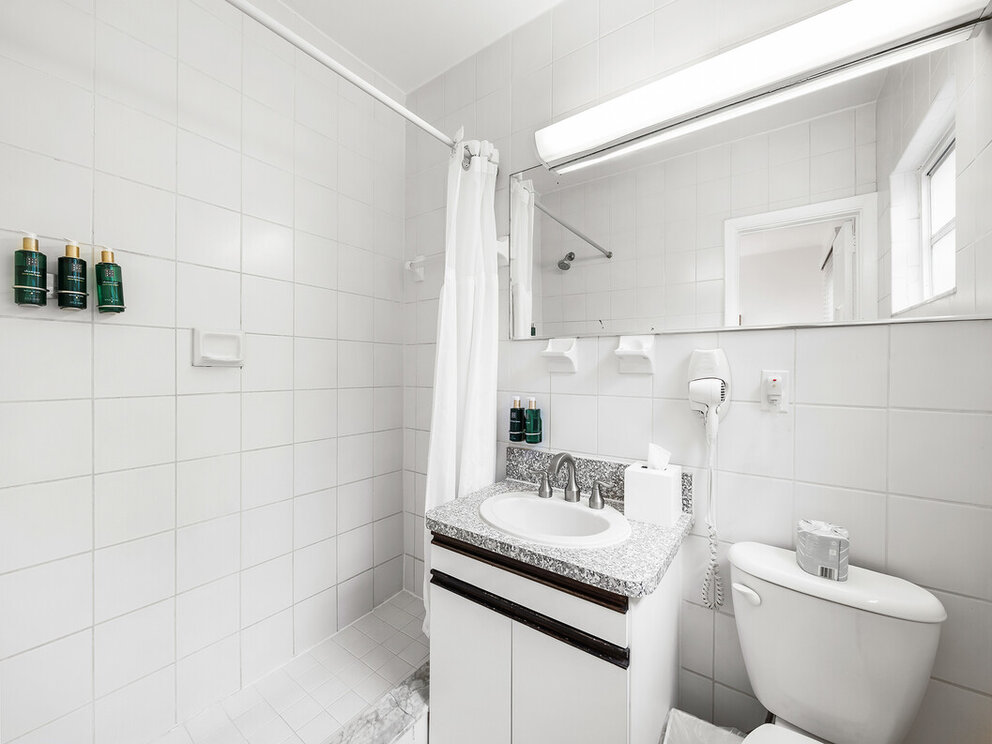 A clean and modern bathroom with white tile, a single sink, toilet, and shower.