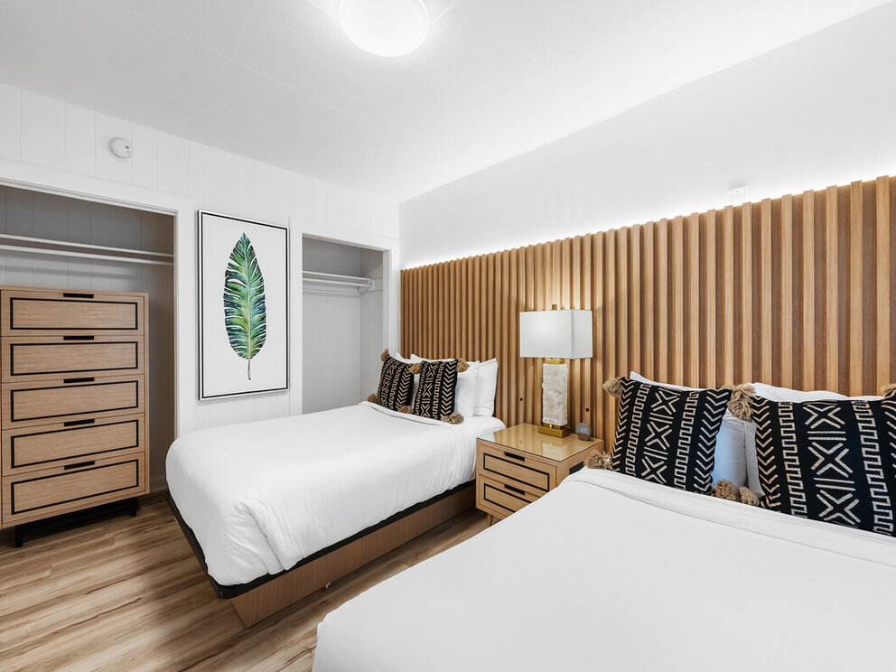 A hotel room with two beds, wooden furniture, and a slatted wood accent wall.