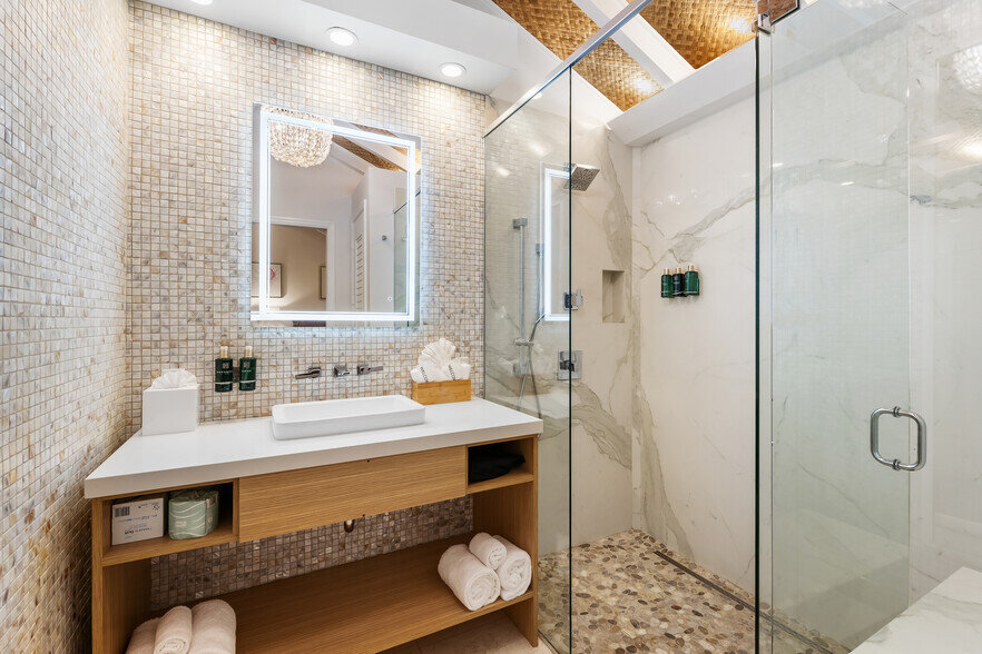 A modern luxury bathroom with a glass-enclosed shower, marble walls, and a wooden vanity.